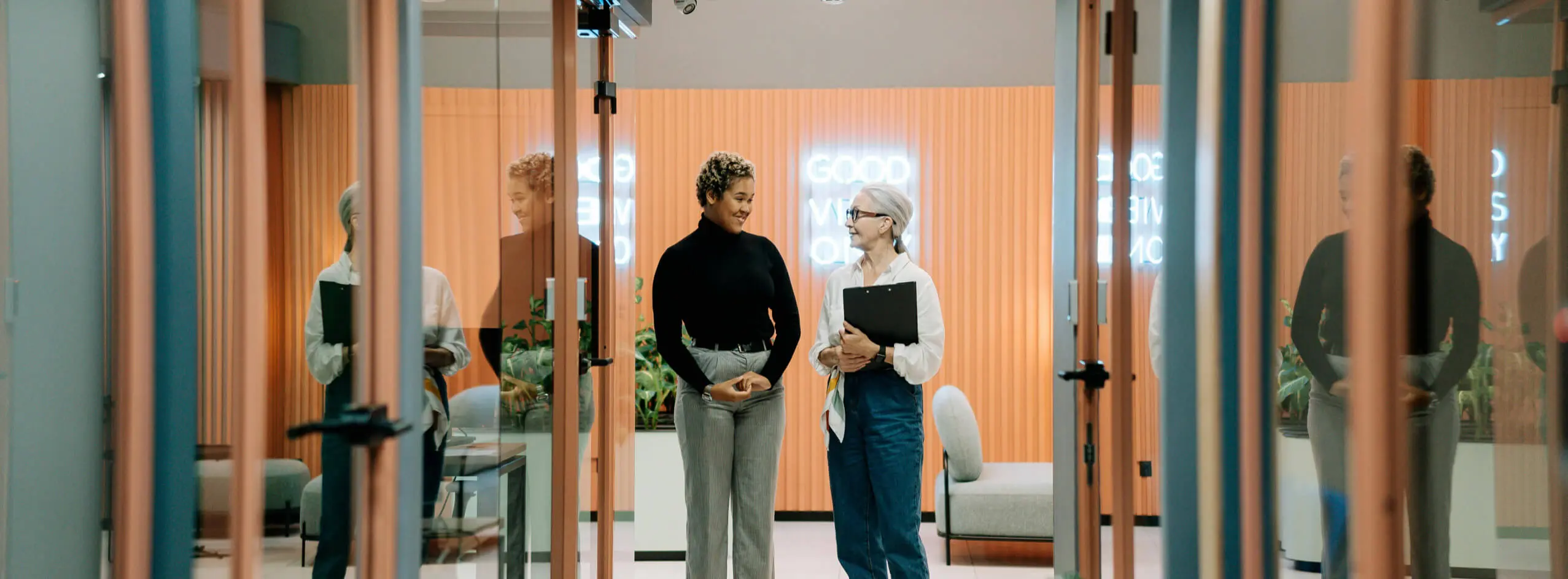 Professional corporate business colleagues walking together and discussing strategies in a modern glass-walled office corridor.