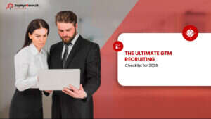 Two recruiters reviewing a laptop beside a title card reading The Ultimate GTM Recruiting Checklist for 2026.