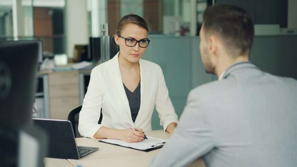 Recruiter taking notes while interviewing a candidate across a desk