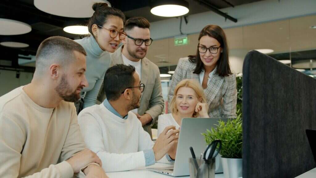 Sales team gathered around a laptop reviewing results in an open-plan office