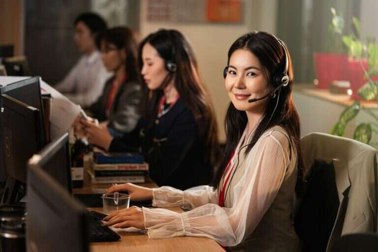 Inside sales representative smiling on a headset on a busy sales floor