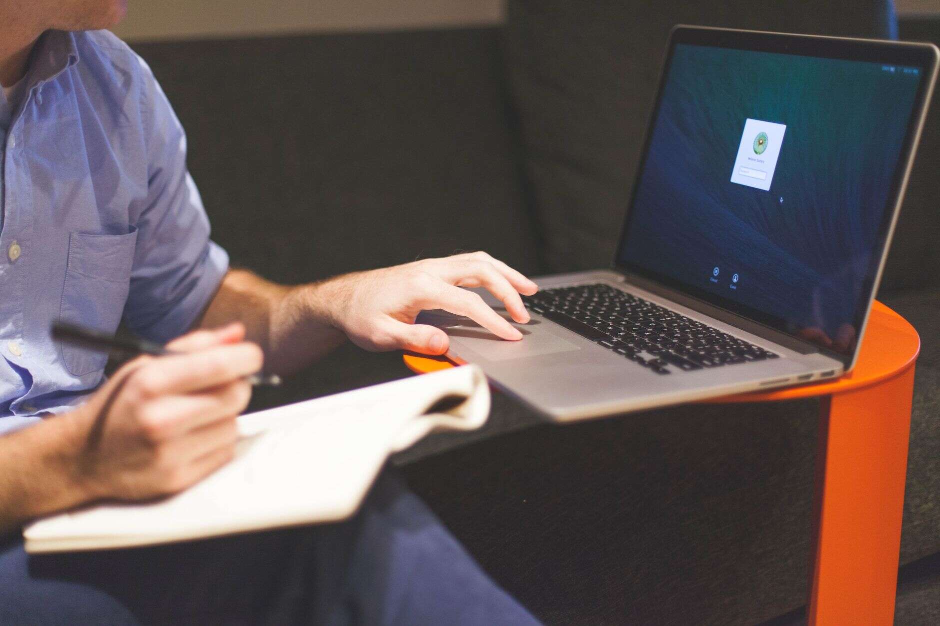 Technical writer taking notes in a notebook beside an open laptop