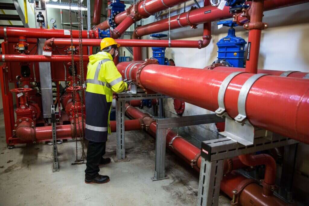 A contractor in hi-vis inspecting red pipework in a plant room