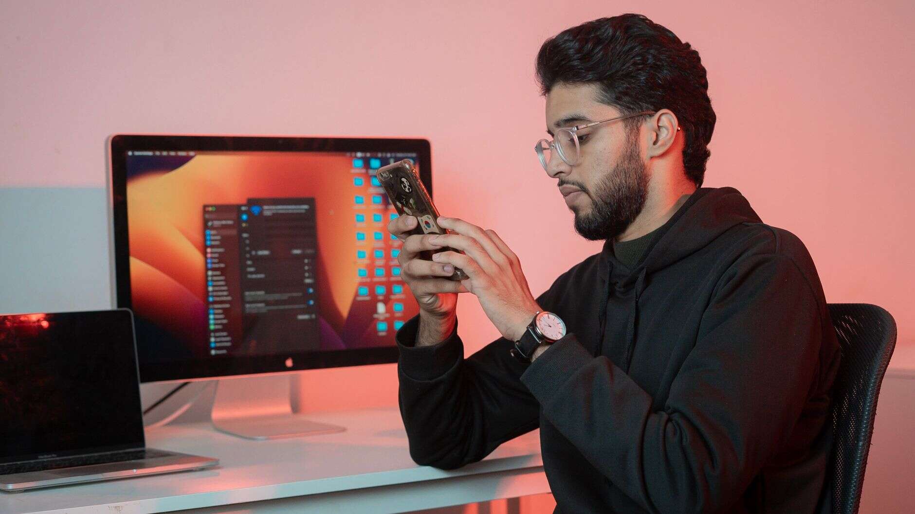 Social media manager checking his phone at a desk beside a computer