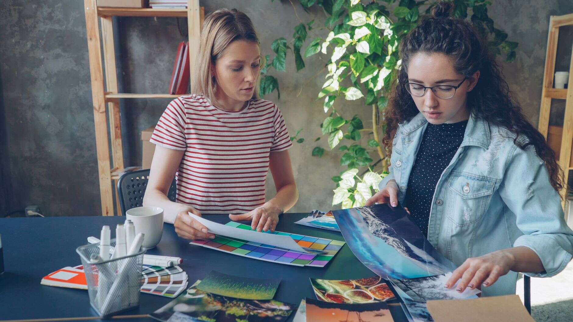 Two graphic designers reviewing printed layouts and color swatches at a shared desk