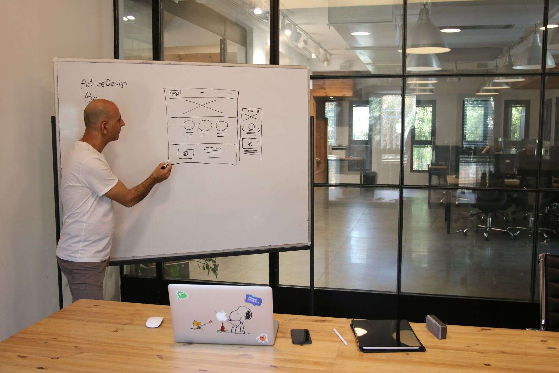 Web designer sketching a page wireframe on a whiteboard in a glass-walled office