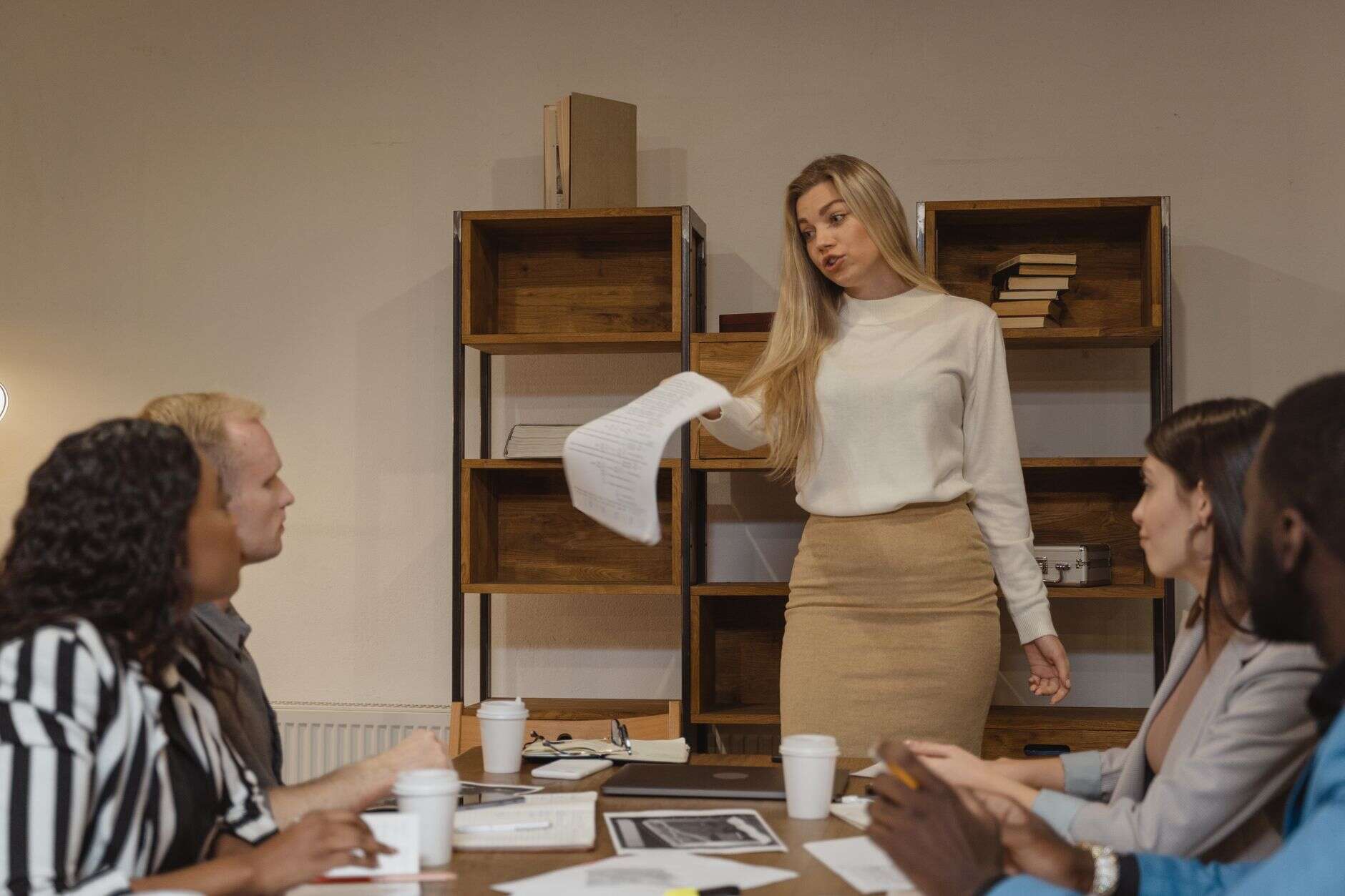 Marketing executive presenting to the team with a paper in hand in a bright meeting room