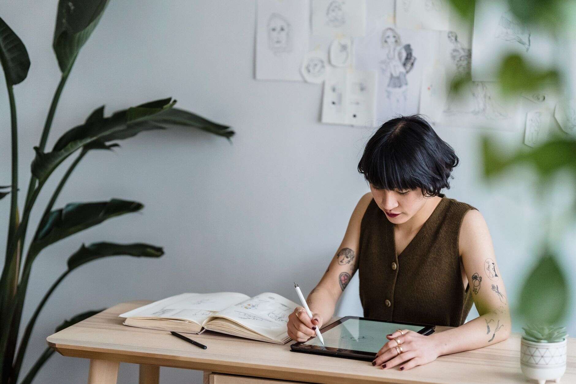 Illustrator drawing on a tablet at a table surrounded by plants and sketches