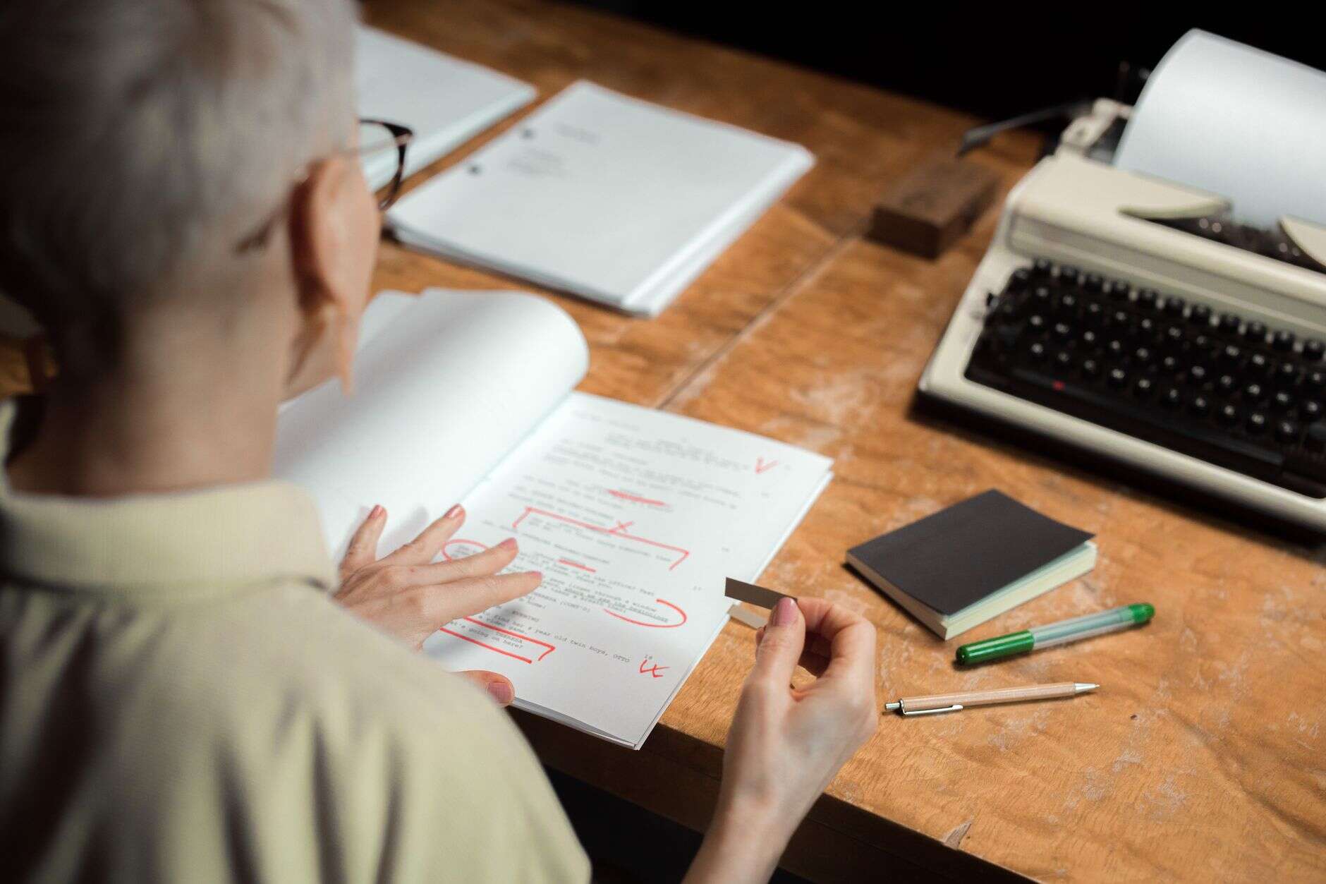 Copywriter reviewing marked-up copy with a red pen at a wooden desk