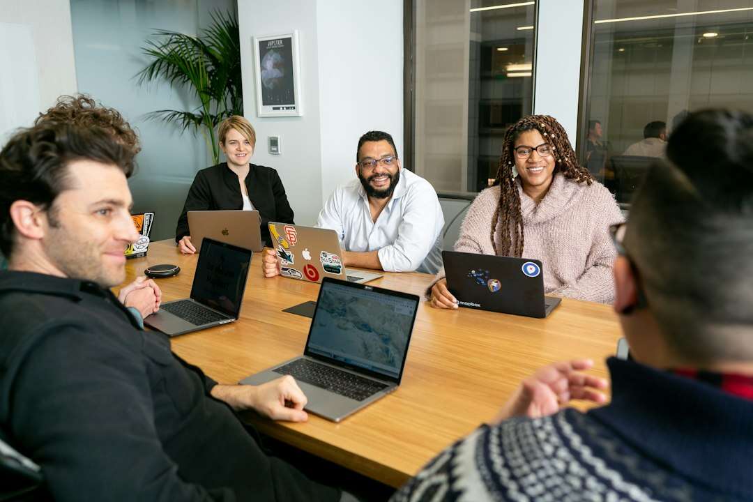 Four colleagues around a meeting table with laptops, smiling as they discuss a hire