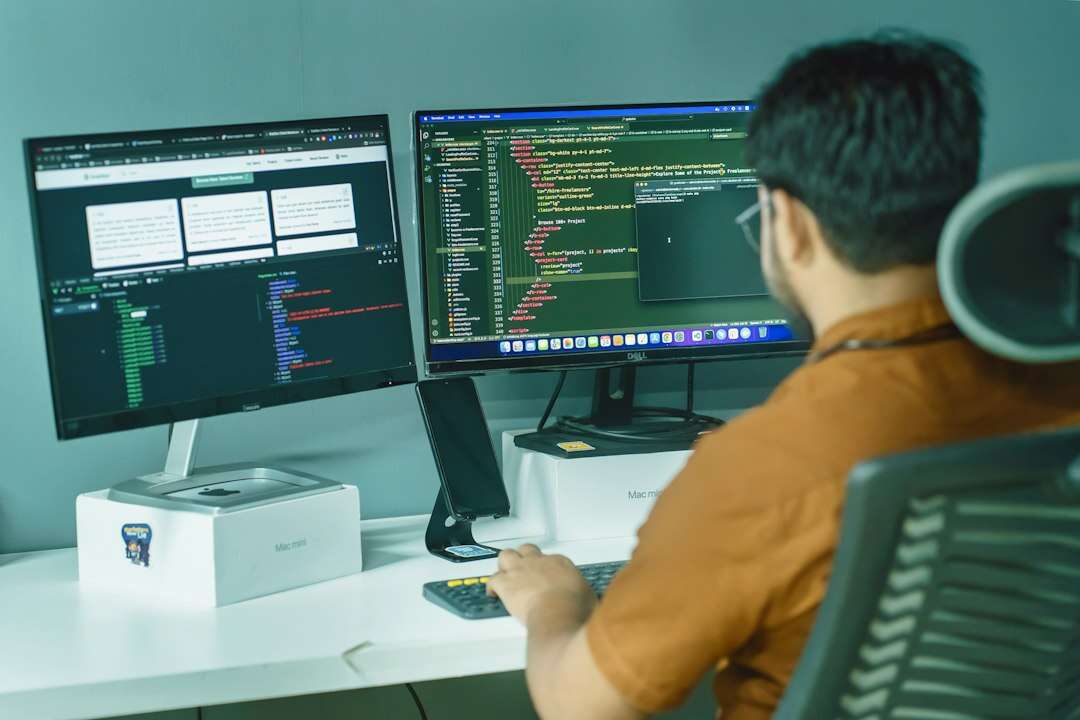 DevOps engineer working across two monitors of code in a teal-walled office