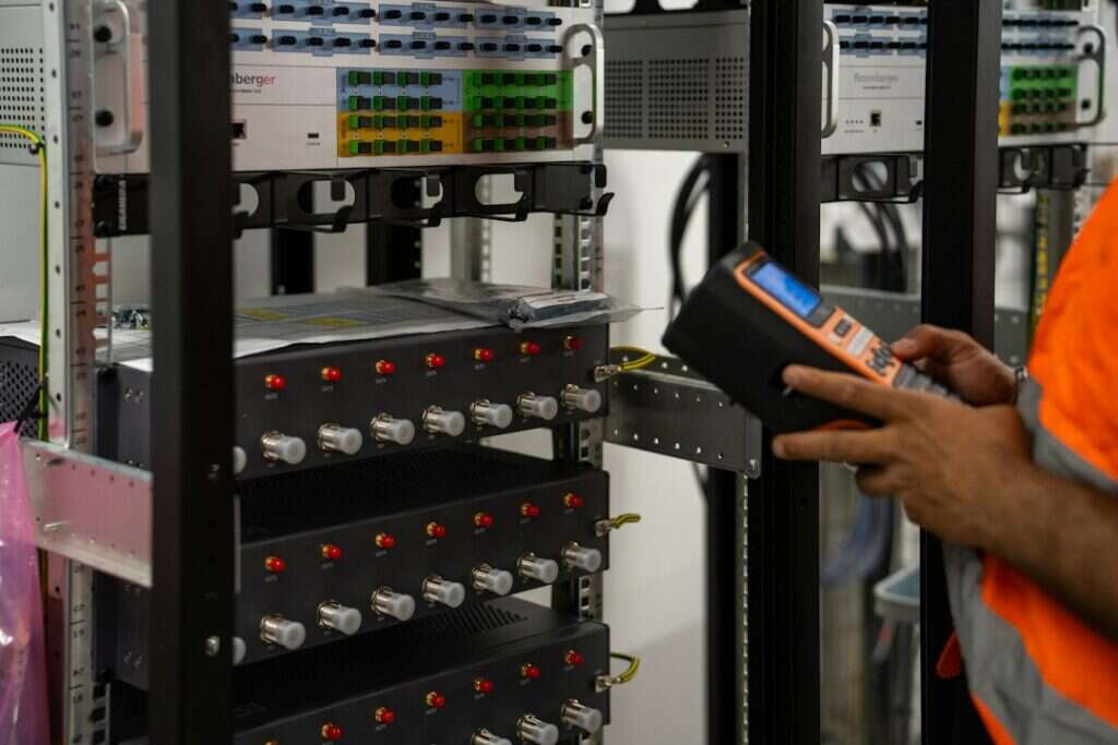 An engineer checking network equipment in a server rack with a handheld tester